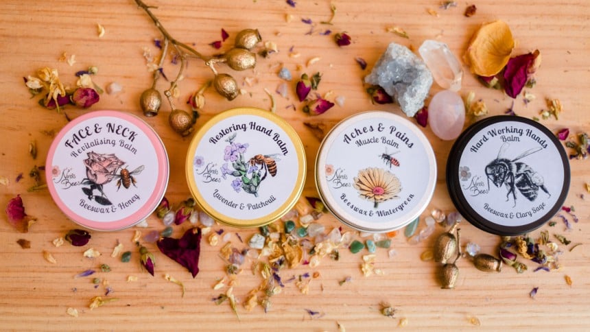 Four round containers with printed labels on the lids. All sitting on a wooden background amongst scattered coloured materials.