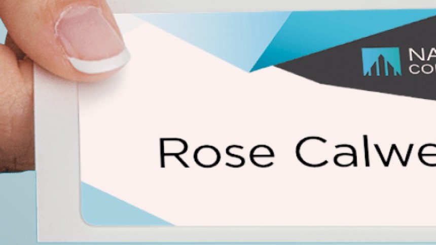 A hand with manicured fingernails holds a name tag that reads "Rose Calwell." The top of the name tag has a modern design with white, gray, and blue geometric shapes and the logo for "National Company."