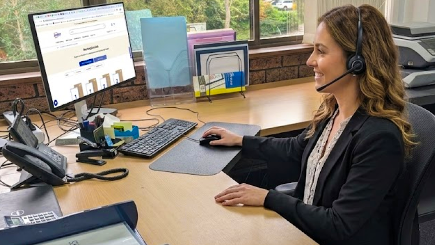 A customer service girl sitting at her desk in the Avery office while on a call using her headset.