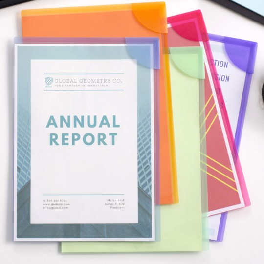 A top-down view of a white desk with a keyboard, a laptop, and a small cup of rubber bands. In the center, a stack of colorful semi-transparent plastic folders holds a document titled "ANNUAL REPORT" for "GLOBAL GEOMETRY CO." The folders are orange, pink, light green, and purple. The "Annual Report" cover page has a blue and green geometric design.