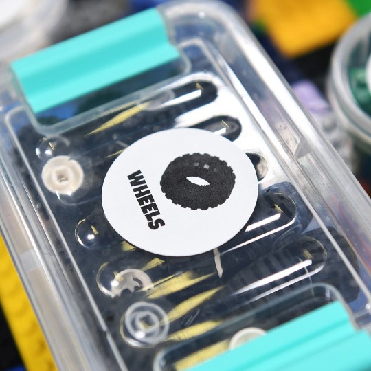 Lego container with lego wheels inside. Round label on top with the image and word wheels printed.