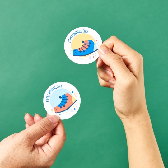 2 hands holding up to round white stickers with colourful print.