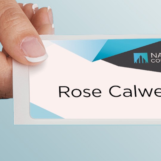 A hand with manicured fingernails holds a name tag that reads "Rose Calwell." The top of the name tag has a modern design with white, gray, and blue geometric shapes and the logo for "National Company."