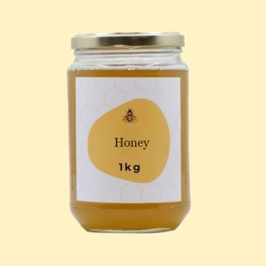 A front view of a large, transparent glass jar of honey with a gold lid. The label is white with a repeating honeycomb pattern. In the center of the label, there is an abstract, golden-yellow shape with a small illustration of a bee and the text "Honey". Below this, the text "1kg" is printed. The jar is set against a plain, light yellow background.