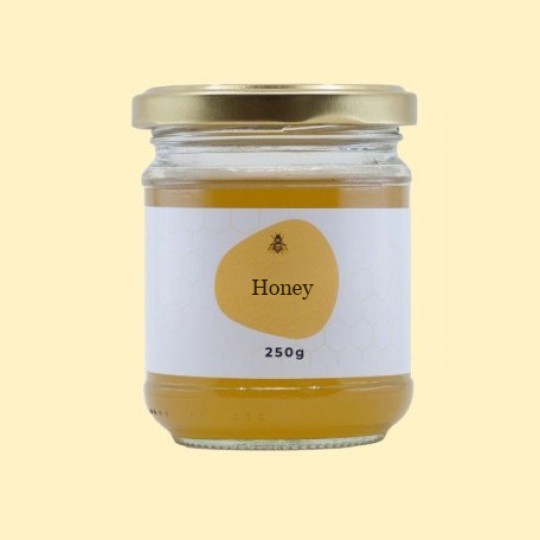 A front view of a short, wide, transparent glass jar of honey with a gold lid. The label is white with a repeating honeycomb pattern. In the center of the label, there is an abstract, golden-yellow shape with a small illustration of a bee and the text "Honey". Below this, the text "250g" is printed. The jar is set against a plain, light yellow background.