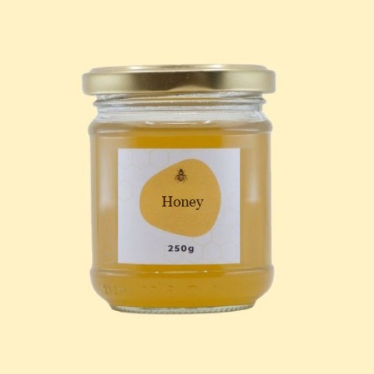 A front view of a short, wide, transparent glass jar of honey with a gold lid. The label is white with a repeating honeycomb pattern. In the center of the label, there is an abstract, golden-yellow shape with a small illustration of a bee and the text "Honey". Below this, the text "250g" is printed. The jar is set against a plain, light yellow background.