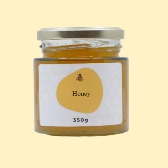 A front view of a short, wide, transparent glass jar of honey with a silver lid. The label is white with a repeating honeycomb pattern. In the center of the label, there is an abstract, golden-yellow shape with a small illustration of a bee and the text "Honey". Below this, the text "350g" is printed. The jar is set against a plain, light yellow background.