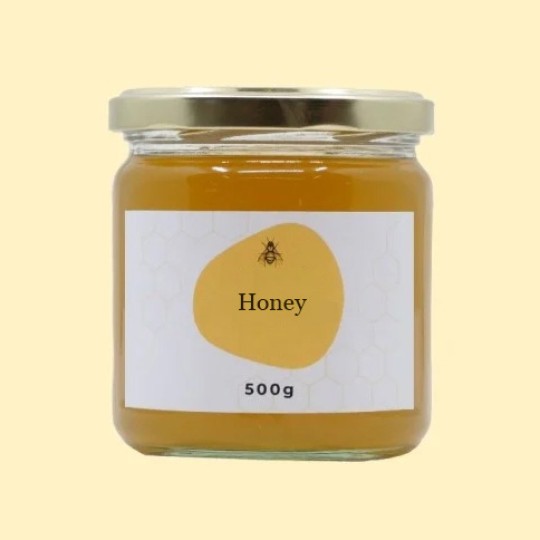 A front view of a small, transparent glass jar of honey with a gold lid. The label is white with a repeating honeycomb pattern. In the center of the label, there is an abstract, golden-yellow shape with a small illustration of a bee and the text "Honey". Below this, the text "500g" is printed. The jar is set against a plain, light yellow background.