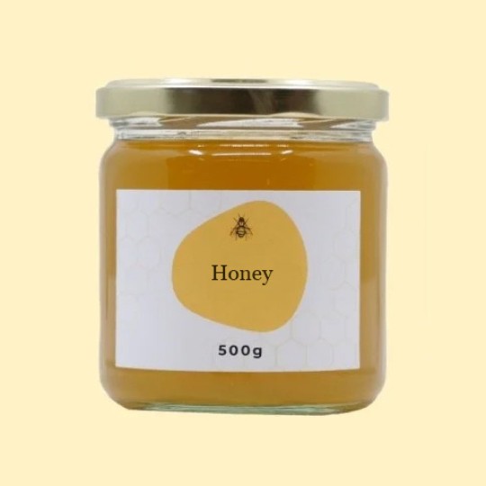 A front view of a small, transparent glass jar of honey with a gold lid. The label is white with a repeating honeycomb pattern. In the center of the label, there is an abstract, golden-yellow shape with a small illustration of a bee and the text "Honey". Below this, the text "500g" is printed. The jar is set against a plain, light yellow background.