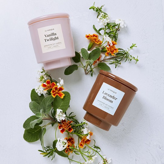 2 candle containers one pink another brown on table with flowers
