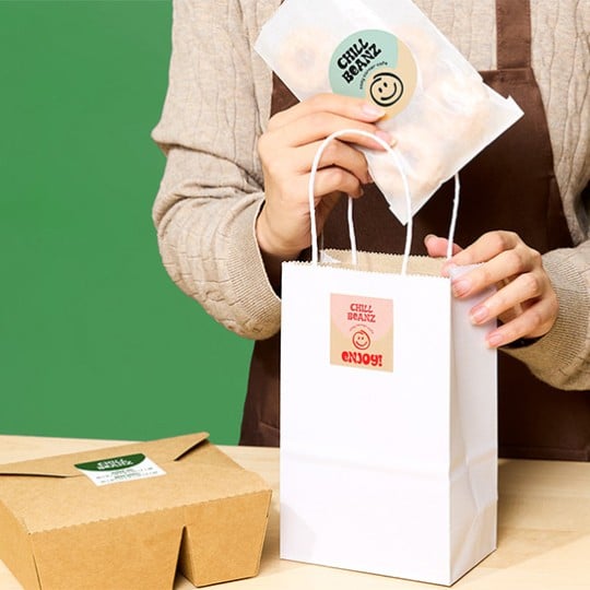 person placing food item in paper bag. both food item and paper bag have a kraft brown label on it