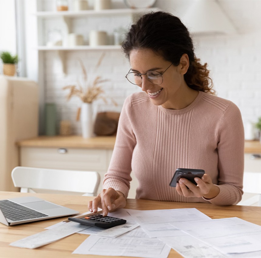 Woman at a desk doing some budgets using a calculator and a laptop.