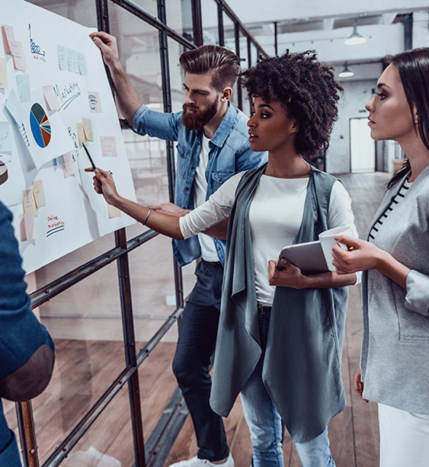 People staring intently and discussing in front of a board of various graphs and post-it notes