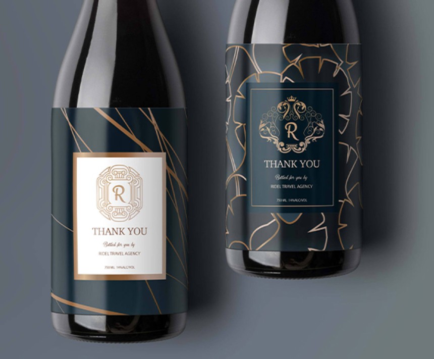 Two dark wine bottles stand side-by-side against a dark gray background, each adorned with elegant, dark teal and gold labels. The bottle on the left features a white central square with a stylized 'R' in a decorative frame, and "THANK YOU" below. The bottle on the right has a dark teal rectangular label with a gold crest, a large 'R', and "THANK YOU" prominently displayed. Both labels also include "Bottled for you by RIDEL TRAVEL AGENCY" and other wine details.