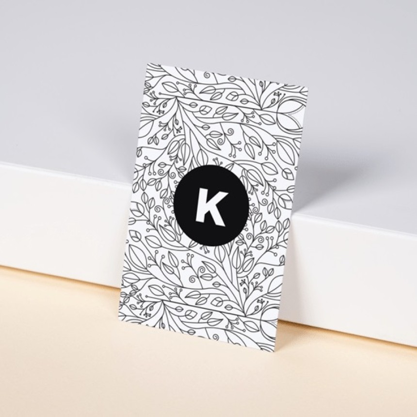 Business Cards leaning against a wall in a portrait position. Simple stylish design with the letter K in the middle of a black circle, and then graphically drawn leaves in background.