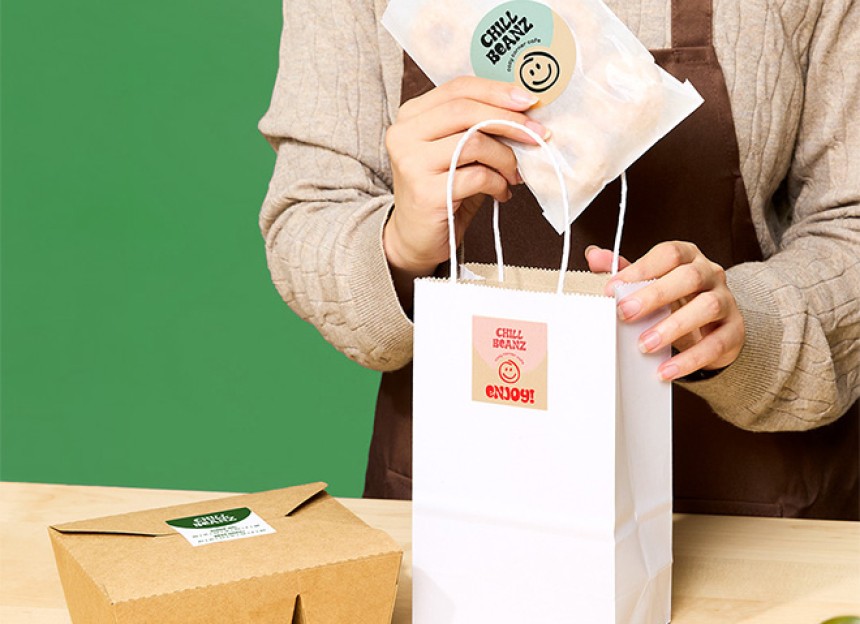 person placing food item into paper bag. both food item and paper bag have a kraft brown label on it