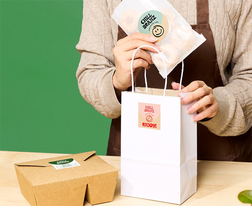 person placing food item in paper bag. both food item and paper bag have a kraft brown label on it