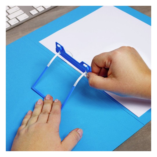 An individual is using a blue document holder clip to secure a white sheet of paper onto a blue folder, with a keyboard visible in the background.
