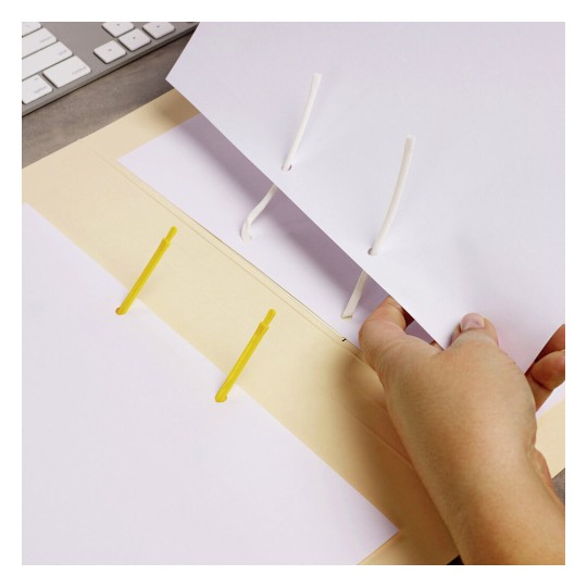 The image shows a person's hand holding a sheet of paper being inserted into a folder with yellow fasteners and white binding cords. A computer keyboard is visible in the background, indicating a workspace setting.