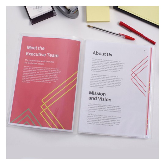 The image displays a document with sections titled 'Meet the Executive Team,' 'About Us,' and 'Mission and Vision.' The pages feature a pink background with geometric designs in yellow and teal. There are also office supplies like a pen, sticky notes, and a stapler in the background.