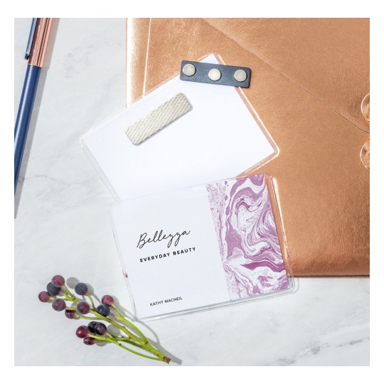 The image features a pink and white marbled card labeled 'Bellezza Everyday Beauty' by Kathy Macneil, alongside a bronze envelope, a pen, and some berries on a light stone surface.
