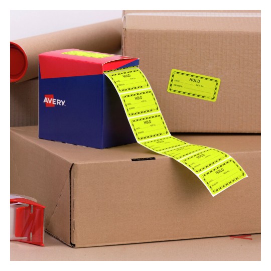 The image depicts a blue and red box labeled 'Avery' with a roll of yellow 'HOLD' labels spilling out. There are cardboard boxes in the background, along with some packing tape.