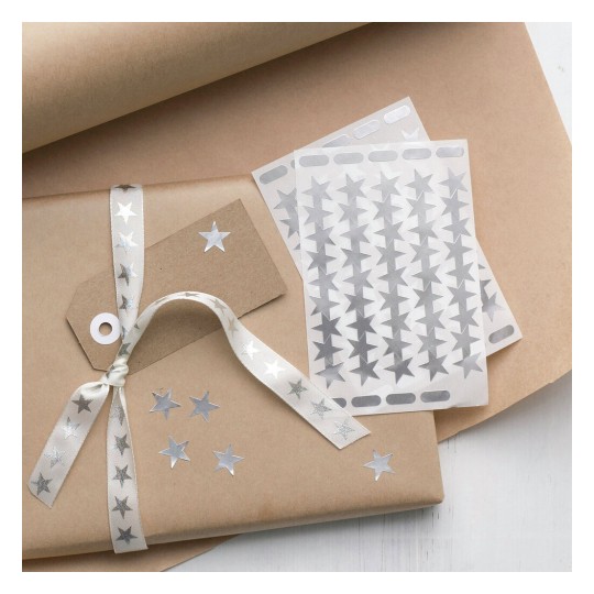 The image features a beautifully wrapped gift in brown paper adorned with silver star stickers and a matching ribbon. There's a gift tag attached, and additional star stickers are placed next to the package.