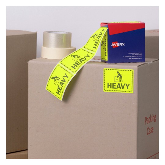 The image shows cardboard boxes with packing tape and bright yellow 'HEAVY' labels. There is also a blue box of Avery products visible, typically used for labeling.