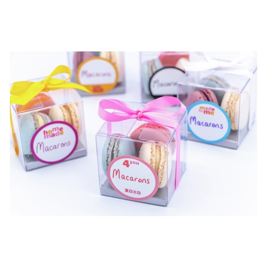 The image features colorful macarons packaged in transparent boxes with decorative ribbons. Each box has a label indicating the contents, such as 'homemade' and 'for you', showcasing an assortment of macarons in various pastel colors.
