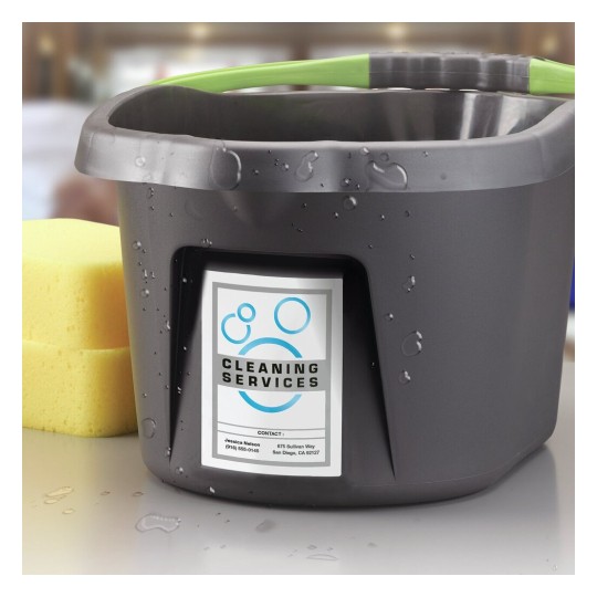 The image shows a gray cleaning bucket with a label indicating cleaning services, along with a yellow sponge beside it. The bucket has water droplets on it, suggesting it's recently been used.