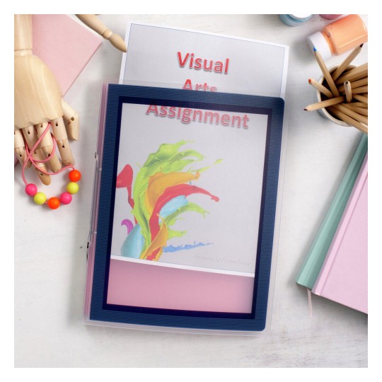 The image features a colorful visual arts assignment folder with vibrant splashes of paint on the cover. Surrounding items include a wooden mannequin, a necklace with colorful beads, colored pencils, paint containers, and stacked books, all arranged on a light-colored surface.