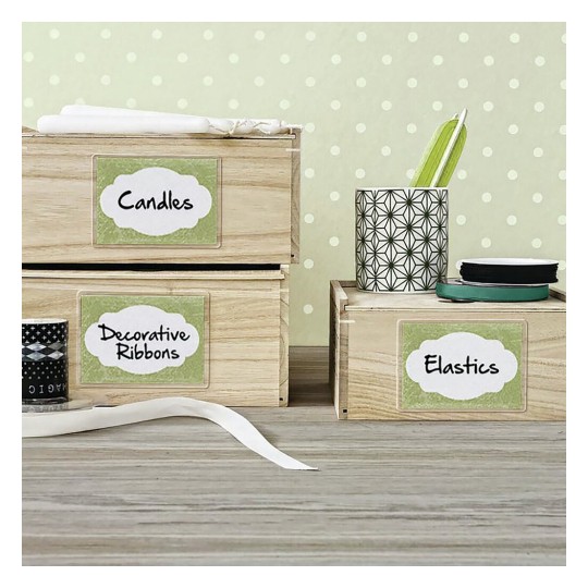 The image shows a neatly organized workspace with wooden boxes labeled 'Candles,' 'Decorative Ribbons,' and 'Elastic.' There’s a decorative cup with pens and various rolls of ribbon nearby, all set against a light polka-dotted background.