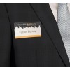 A close-up shot of a man in a dark blue suit jacket and a light blue patterned tie. A clear name badge with a white and orange section is pinned to his lapel. The top of the badge features a dark cityscape silhouette and the text "WILLIAMS&BRAUN REAL ESTATE SERVICES." The bottom of the badge is white with a thin orange stripe at the bottom, and the name "Fabian Barros" is written in black text.