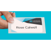 A hand with manicured fingernails holds a name tag that reads "Rose Calwell." The top of the name tag has a modern design with white, gray, and blue geometric shapes and the logo for "National Company."