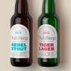 2 beer bottles lying on plain background. Each bottle has an arched label with the brands logo and product title