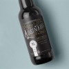 Black beer bottle laying down on a blue table with a grey label on the bottle
