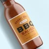 Jar of bbq sauce laying flat on a blue background with an orange label on the jar