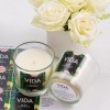 2 glass candle jars. One standing up, the other lying down. Floral labels attached to both jars. A bouquet of flowers in the background.