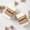 2 artisan soap bars on a table surrounded by flowers. They have a kraft wrap with a kraft label with the words oatmeal and almond soap