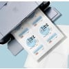 A close-up, high-angle shot of a printer ejecting a sheet of paper with multiple wine bottle labels printed on it. The labels are predominantly white and light blue with black text, featuring "HAUS" as a prominent brand name, "MALBEC," "NAPA VALLEY, CA," and other wine details. Partially visible blank label sheets are stacked below.