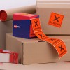 The image features cardboard boxes along with a box of labels. One label reads 'REJECTED' in bold on an orange background. There is packing tape visible, and the scene suggests packaging or shipping activities.