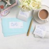 The image shows a collection of envelopes with addresses written on them, a gold pen, a cup of tea or coffee, and a small bouquet of white roses. The background features a light-colored wooden surface.