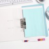 The image shows an open binder with a light blue sheet of paper inside, along with various office supplies such as a computer keyboard, a mouse, and a bowl of clips. The workspace is organized and minimalistic.