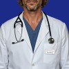 The image shows a man in a white lab coat with a stethoscope. He has a blue scrub underneath and a name tag on his coat pocket.