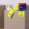 The image shows cardboard boxes with packing tape and bright yellow 'HEAVY' labels. There is also a blue box of Avery products visible, typically used for labeling.