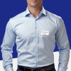 The image features a man wearing a light blue dress shirt with a name badge. The background is a solid blue, and the individual appears to be in a professional setting.