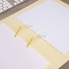 The image shows an open binder with white pages, secured by yellow and white rings, placed on a wooden surface next to a computer keyboard.