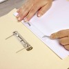 A close-up of hands placing a white paper into a folder, with a metal binder clip visible. The hands are interacting with the folder and paper.